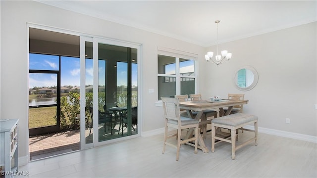 dining space with ornamental molding, a water view, baseboards, and an inviting chandelier