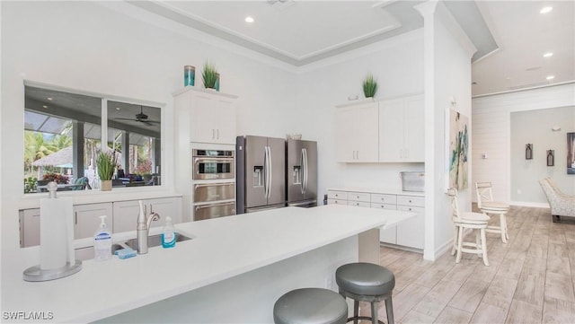 kitchen with stainless steel appliances, light countertops, white cabinetry, light wood-type flooring, and a kitchen bar