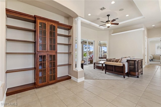 living room featuring ceiling fan, a tray ceiling, light tile patterned floors, and ornate columns