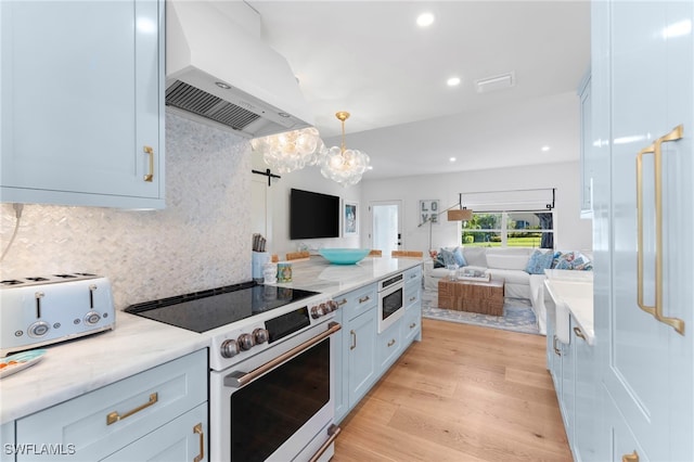 kitchen with built in microwave, light stone counters, decorative light fixtures, range hood, and high end stove