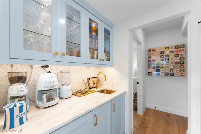 bar featuring blue cabinets, sink, light stone counters, and light wood-type flooring