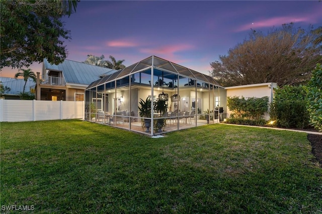 back house at dusk with a lawn, a patio, and glass enclosure