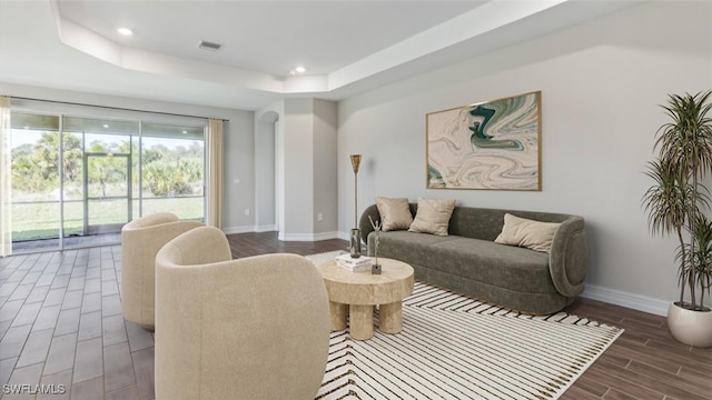 living area with a tray ceiling, visible vents, baseboards, and wood finish floors