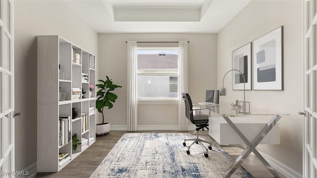 office area with wood finish floors, a raised ceiling, and baseboards