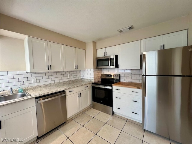 kitchen featuring sink, appliances with stainless steel finishes, white cabinetry, backsplash, and light tile patterned flooring