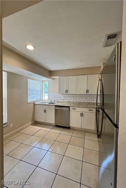 kitchen with light tile patterned floors, sink, appliances with stainless steel finishes, white cabinets, and decorative backsplash