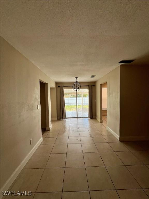 spare room with a notable chandelier, a textured ceiling, and light tile patterned flooring