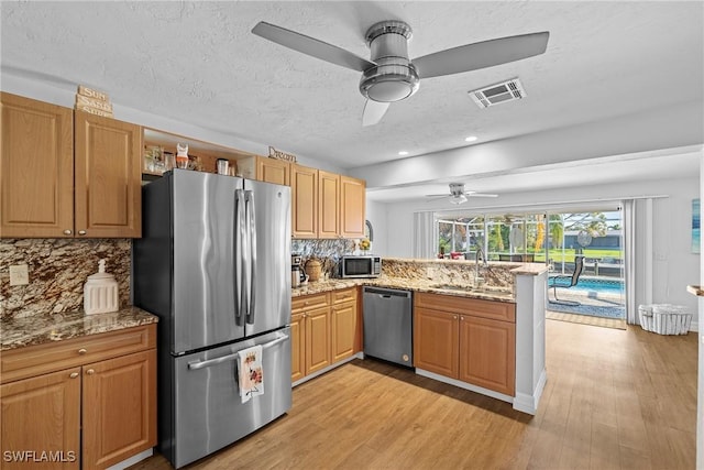 kitchen featuring sink, kitchen peninsula, stainless steel appliances, light stone countertops, and light hardwood / wood-style floors