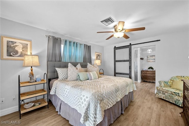 bedroom with ceiling fan, a barn door, and light hardwood / wood-style flooring