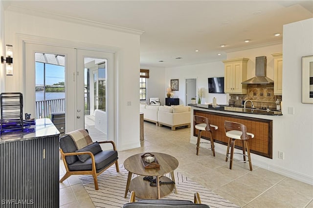 kitchen featuring decorative backsplash, light tile patterned floors, crown molding, a water view, and wall chimney range hood