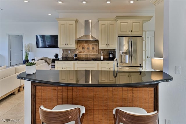 kitchen with tasteful backsplash, stainless steel fridge with ice dispenser, light tile patterned floors, cream cabinets, and wall chimney range hood