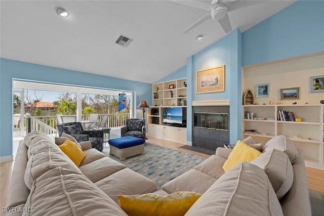 living room featuring built in shelves, a fireplace, light wood finished floors, visible vents, and high vaulted ceiling