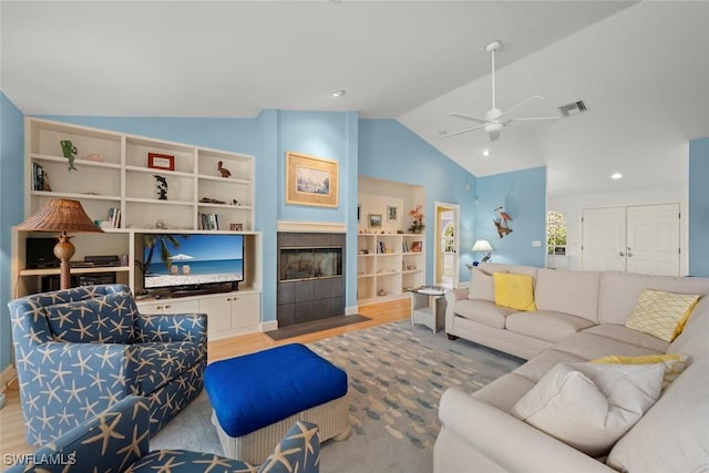 living room featuring visible vents, a ceiling fan, vaulted ceiling, light wood finished floors, and a tiled fireplace