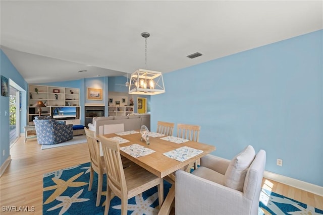 dining room with visible vents, lofted ceiling, light wood-style flooring, an inviting chandelier, and a fireplace