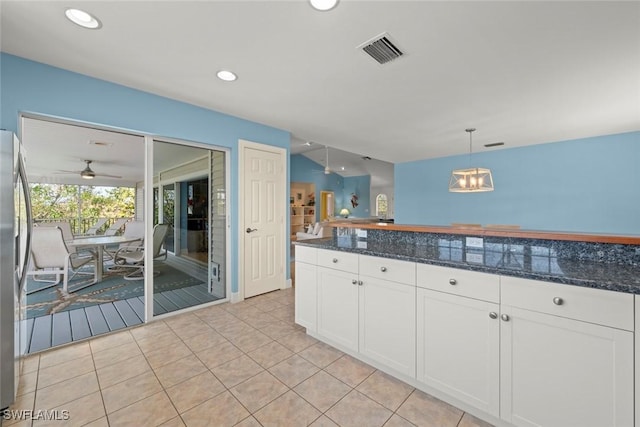 kitchen with light tile patterned floors, visible vents, dark stone countertops, decorative light fixtures, and white cabinetry