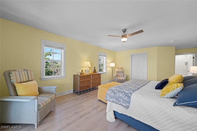 bedroom featuring light wood finished floors, multiple windows, a ceiling fan, and baseboards