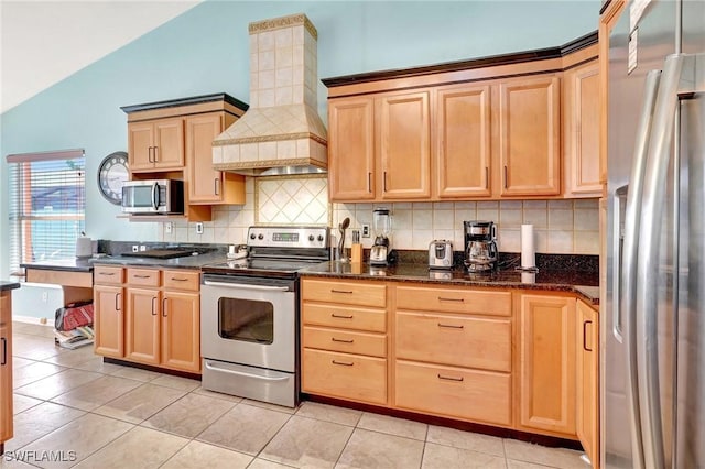 kitchen featuring light brown cabinets, custom exhaust hood, vaulted ceiling, appliances with stainless steel finishes, and tasteful backsplash