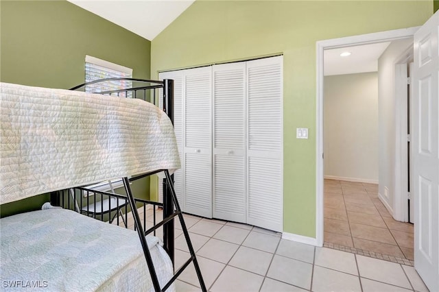 bedroom featuring light tile patterned flooring, baseboards, a closet, and vaulted ceiling