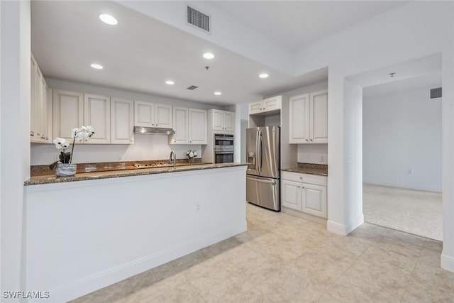 kitchen with white cabinetry, appliances with stainless steel finishes, kitchen peninsula, and dark stone counters