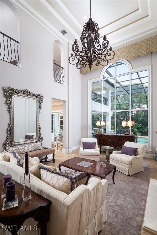 living room with a tray ceiling, ornamental molding, a notable chandelier, and a towering ceiling