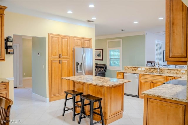 kitchen with a kitchen bar, sink, a center island, stainless steel appliances, and light stone countertops