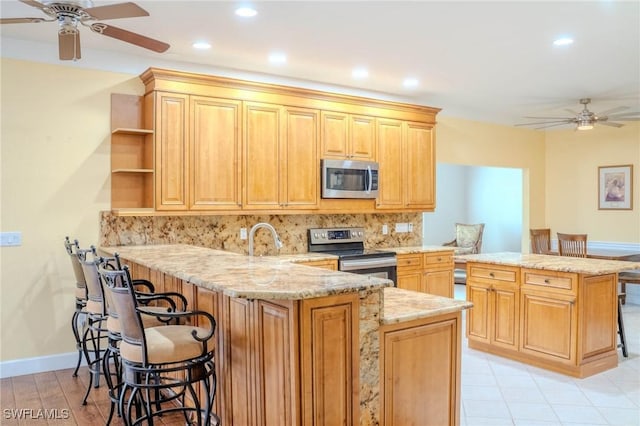 kitchen featuring appliances with stainless steel finishes, backsplash, light stone countertops, a kitchen bar, and kitchen peninsula