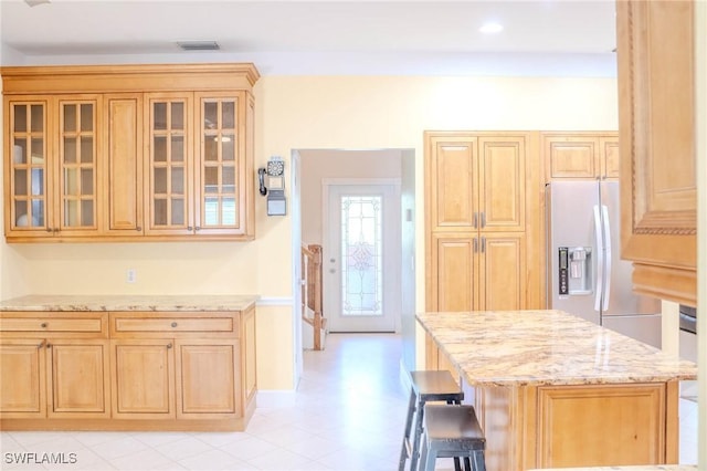 kitchen with stainless steel refrigerator with ice dispenser, a breakfast bar area, and light stone counters