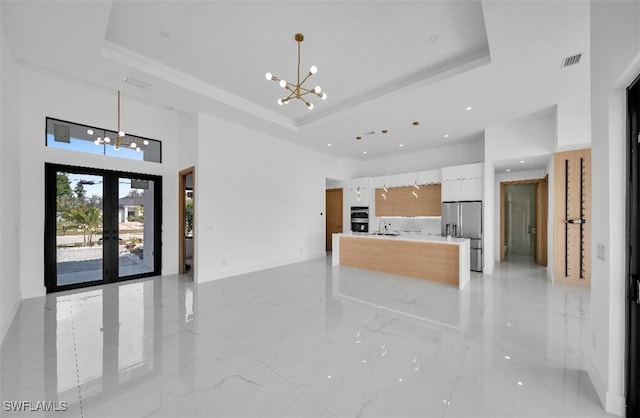 kitchen with pendant lighting, white cabinetry, stainless steel fridge, a notable chandelier, and a raised ceiling