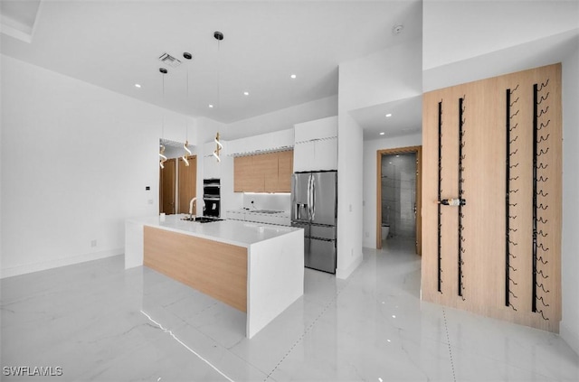 kitchen with sink, a center island with sink, hanging light fixtures, stainless steel appliances, and white cabinets