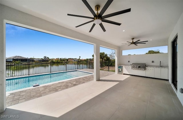 view of pool with a patio, an outdoor kitchen, a grill, sink, and a water view