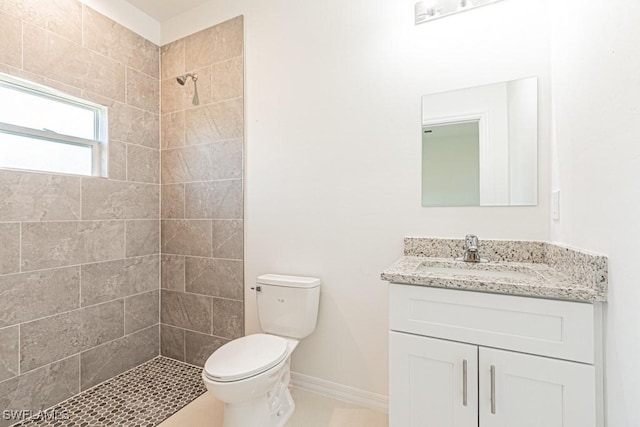 full bath featuring toilet, baseboards, tiled shower, and vanity