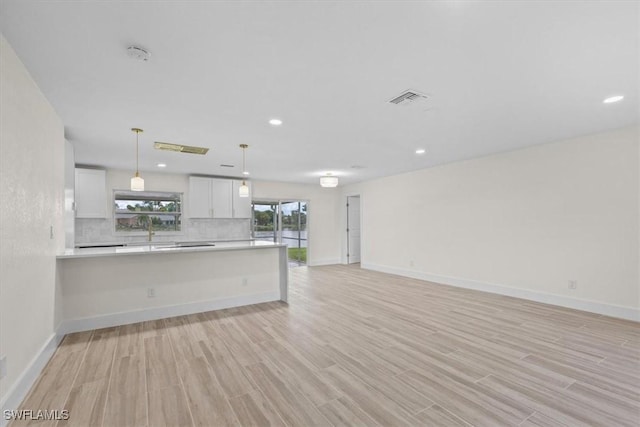 kitchen with light hardwood / wood-style flooring, pendant lighting, white cabinets, and decorative backsplash