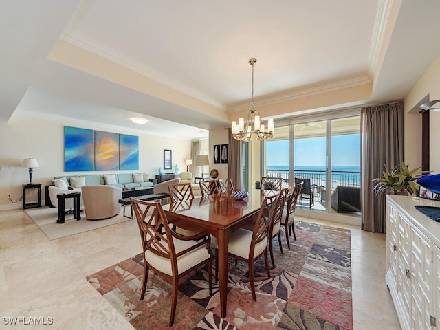 dining space with a water view, ornamental molding, a tray ceiling, and an inviting chandelier