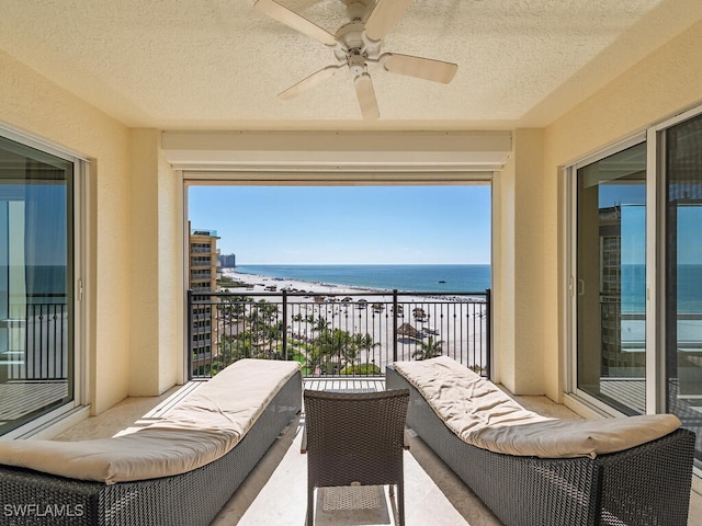 balcony with a beach view, ceiling fan, and a water view