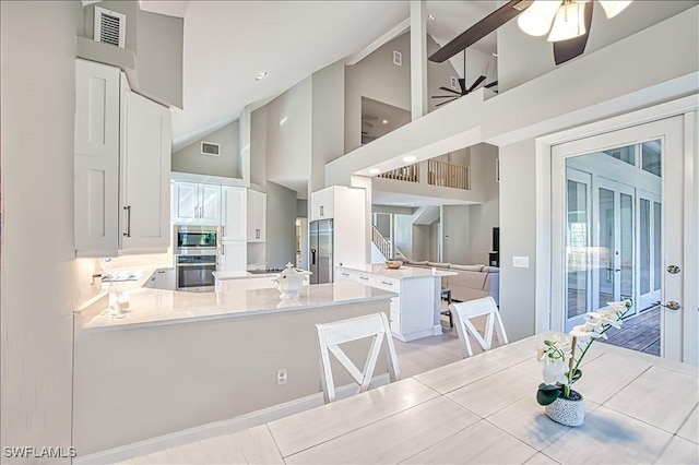 kitchen featuring appliances with stainless steel finishes, high vaulted ceiling, white cabinets, a kitchen bar, and kitchen peninsula