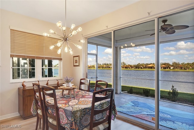 dining room with ceiling fan with notable chandelier, a water view, light hardwood / wood-style flooring, and a healthy amount of sunlight