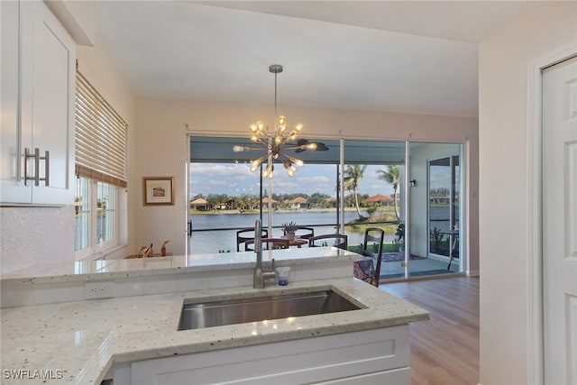 kitchen with a water view, white cabinetry, light stone countertops, and decorative light fixtures