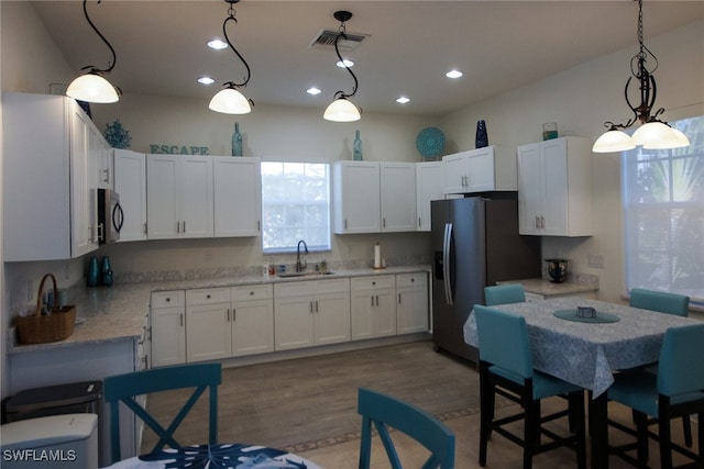 kitchen with sink, stainless steel refrigerator with ice dispenser, white cabinets, hanging light fixtures, and light stone countertops