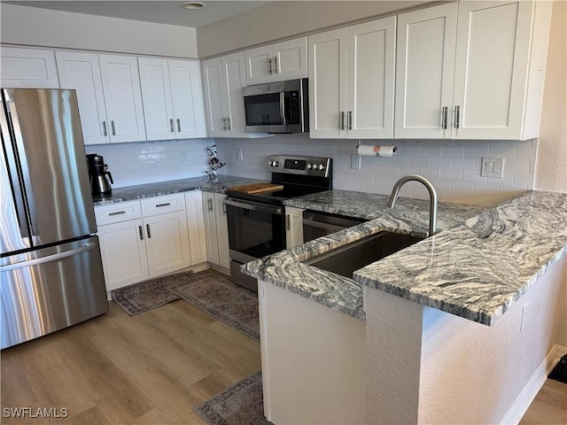 kitchen with light stone counters, a sink, light wood-style flooring, a peninsula, and appliances with stainless steel finishes