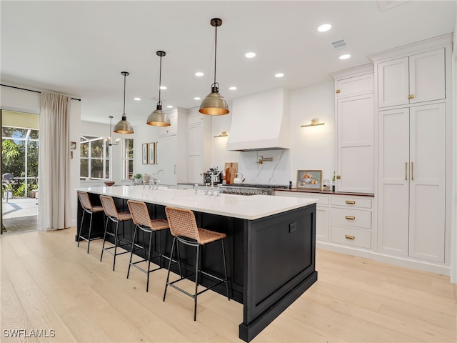 8850 Springwood Ct, Bonita Springs, FL 34135 - kitchen featuring white cabinetry, light wood-style flooring, a large island with sink, and custom exhaust hood