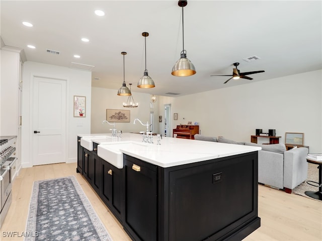 8850 Springwood Ct, Bonita Springs, FL 34135 - kitchen featuring an island with sink, visible vents, light wood-style floors, and dark cabinetry