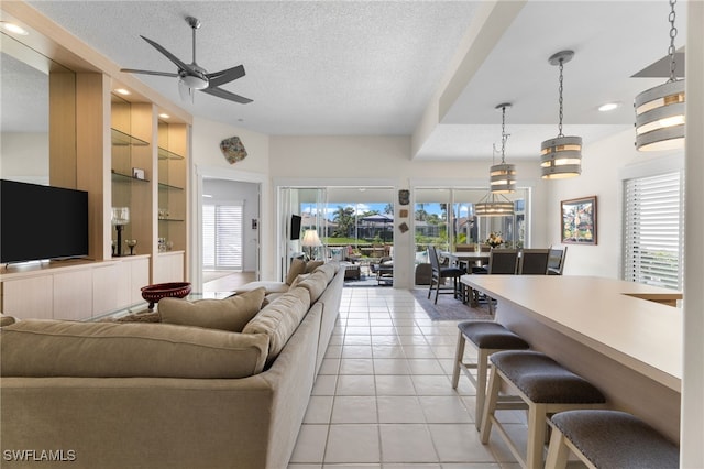 tiled living room featuring ceiling fan, plenty of natural light, built in features, and a textured ceiling