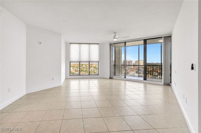 spare room with ceiling fan, a wall of windows, and light tile patterned floors