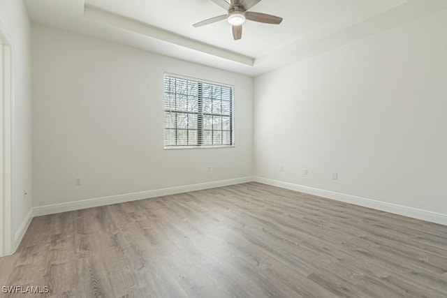 spare room featuring a raised ceiling, ceiling fan, and light wood-type flooring