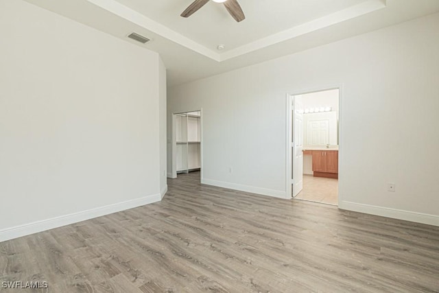 unfurnished room featuring ceiling fan, a tray ceiling, and light hardwood / wood-style flooring