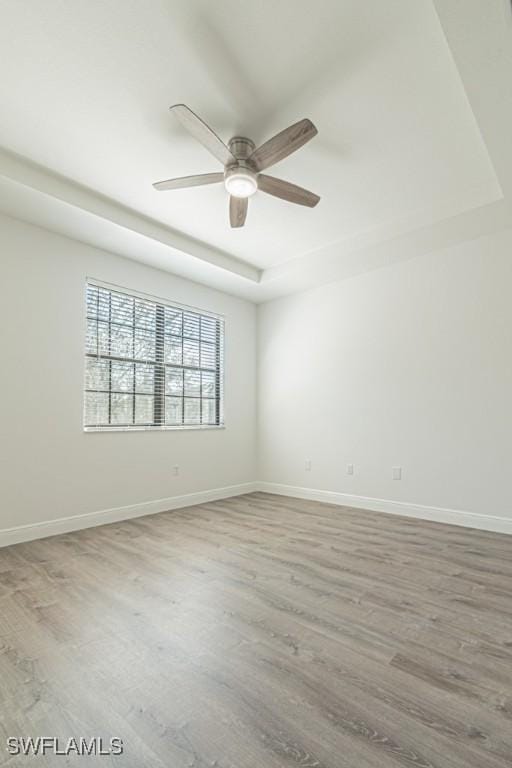 empty room featuring a raised ceiling, hardwood / wood-style flooring, and ceiling fan