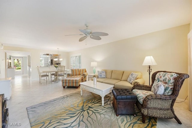 living area with ceiling fan with notable chandelier, light tile patterned flooring, and baseboards