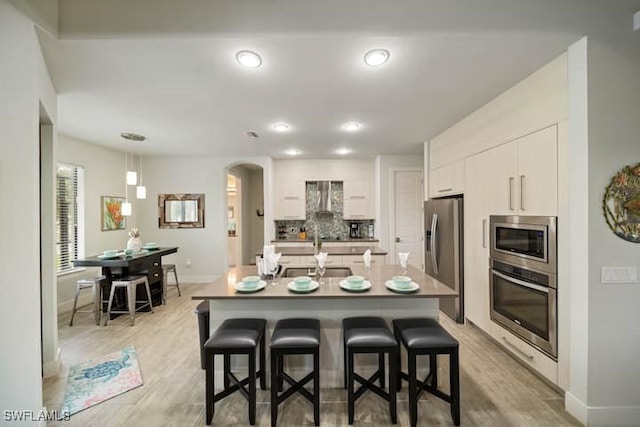 kitchen featuring white cabinetry, a breakfast bar area, hanging light fixtures, a kitchen island with sink, and stainless steel appliances