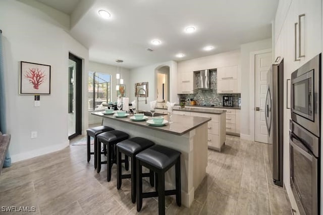 kitchen featuring an island with sink, white cabinetry, a kitchen breakfast bar, decorative backsplash, and stainless steel appliances