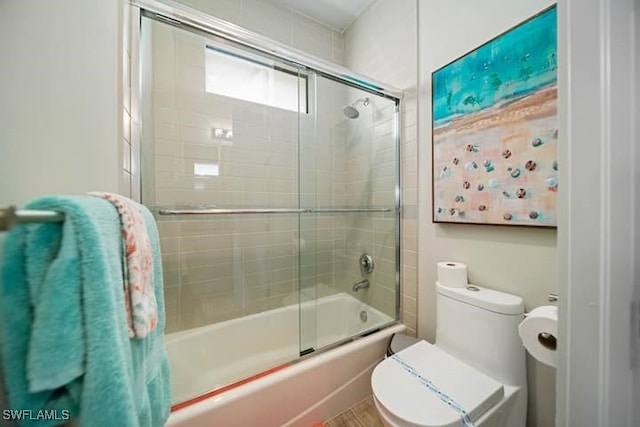 bathroom with toilet and shower / bath combination with glass door